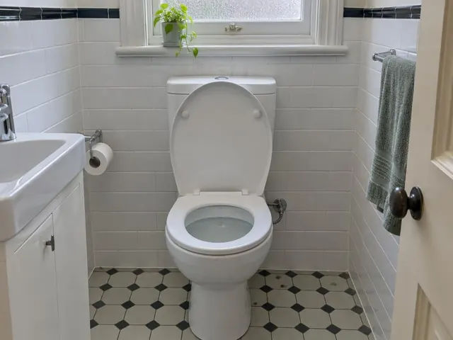 Clean white toilet in a tiled bathroom with sink, towel rail and window in Lewisham