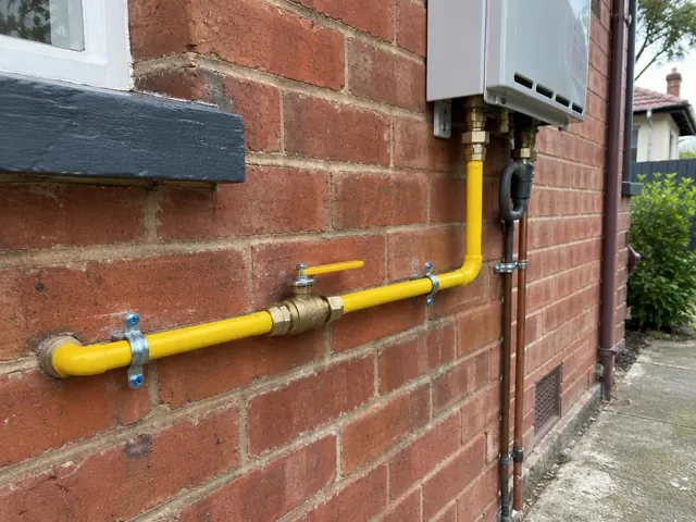 Yellow gas pipe and new fittings on a brick exterior wall beside a window and utility unit in Stanmore
