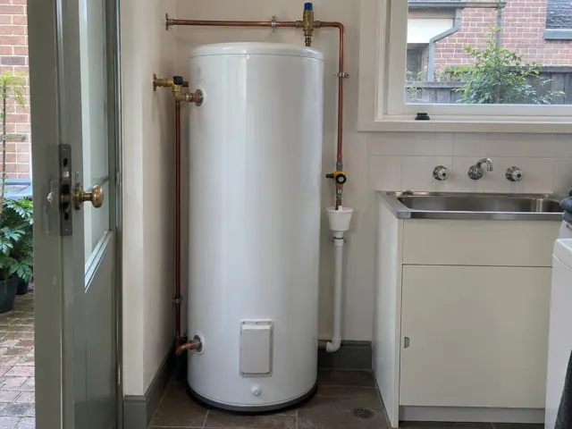 White hot water cylinder beside a sink in a tiled laundry room with copper pipework in Dulwich Hill
